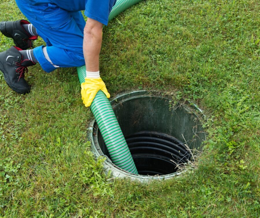 A Martin Environmental technician guides the pump hose into an opened septic tank.